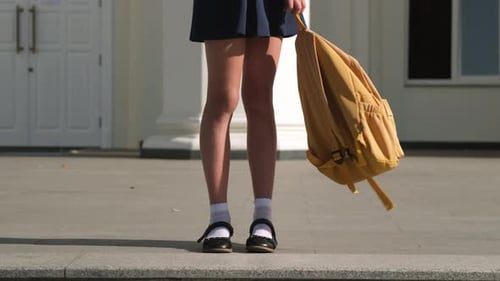 Teen Girl Student Playing with Yellow Backpack on Background of School Building