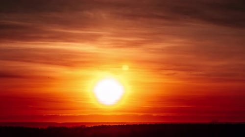 Sonnenuntergang im Zeitraffer mit Linseneffekt am orangefarbenen Himmel durch weiche Wolken über dem Horizont