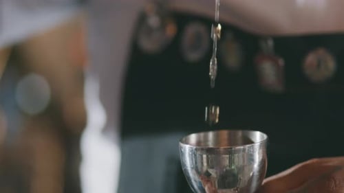 Nahaufnahme einer alkoholischen Flüssigkeit, die in einen Cocktail-Jigger gegossen wird.