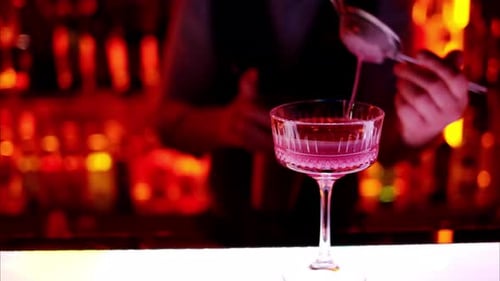 Barman making a cocktail with white sparkling wine at the bar at night with red neon lights, slow mo