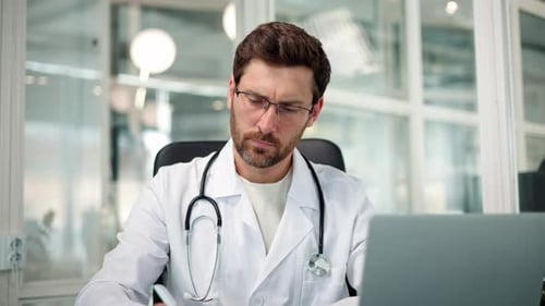 Male Doctor Studying Medical Report of Patient in Office Medical Papers