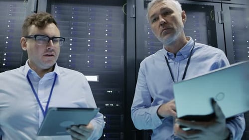 Two Men Working in a Server Room with Tablets