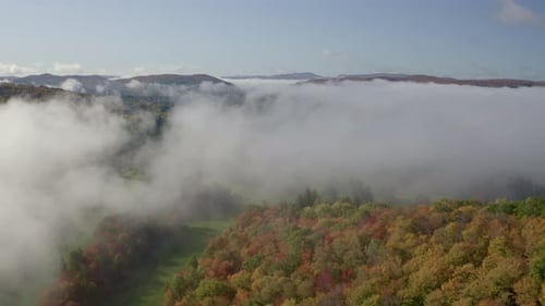 Drone footage showcasing rolling hills adorned with vibrant autumn foliage, blanketed in mist. The s