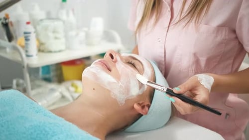 Esteticista que aplica un tratamiento facial en un salón de belleza a una mujer joven.