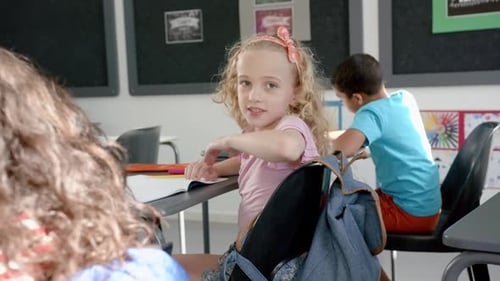 Caucasian girl with blonde curly hair smiles in a classroom setting in school