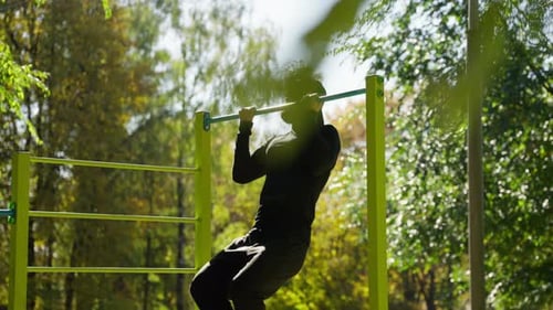 Un hombre hace flexiones en una barra horizontal en el parque