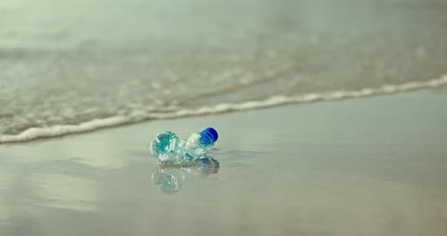 Bottle, beach and waste with pollution for global warming, hazard or recyclable plastic on ocean