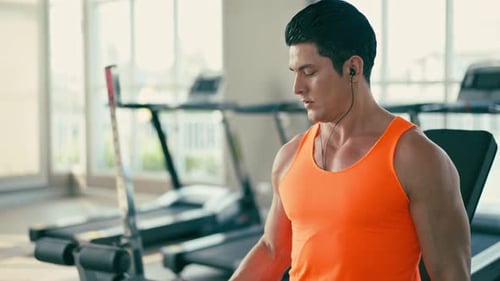 Man Lifting Dumbbell in Gym Wearing Earbuds