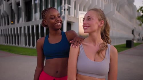 Zwei glückliche und vielfältige Sportlerinnen, die sich nach einer Trainingseinheit in einer urbanen Stadt umarmen und lächeln