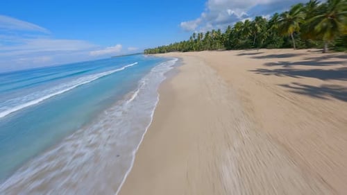 FPV aerial flies low along turquoise blue waves crashing on golden sandy cove of Coson Beach Samana