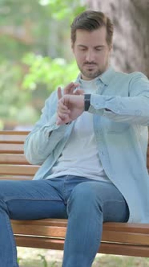 Man Using Smartwatch on Park Bench, Daytime