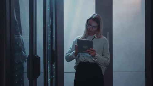 Woman Inspecting Servers with Tablet in Data Center