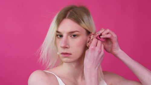 Person putting on earring in front of pink background