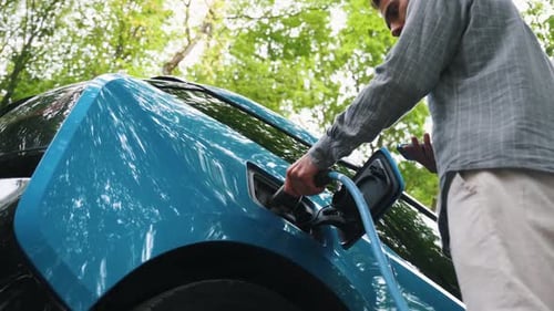 Young man charging electric car outdoor at green forest. Save ecology alternative energy sustainable