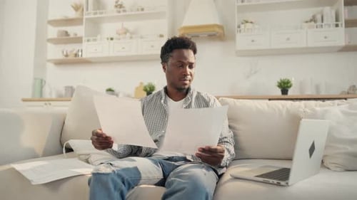 Young Man Reviews Papers with Laptop at Home