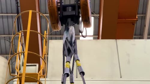 Close-up shot of a heavy-duty crane hook and steel wire slings inside an industrial facility.