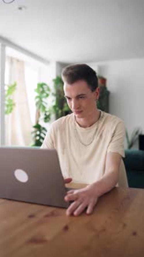 Young Man Typing on Laptop at Wooden Table Indoors