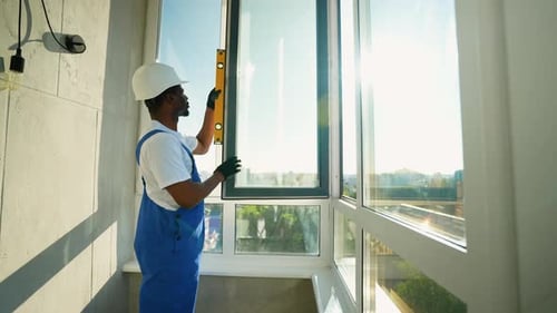 Afroamerikanischer Installateur verwendet eine Ebene, um einen Fensterrahmen genau auszurichten
