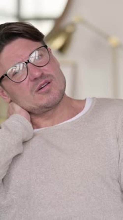 Man in Glasses Massaging His Aching Neck Indoors