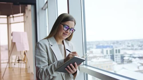Woman Writing in Notebook by Office Window