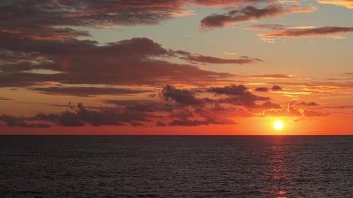 Golden Sunrise Over Calm Sea with Bright Red and Pink Clouds Reflecting on the Water Surface