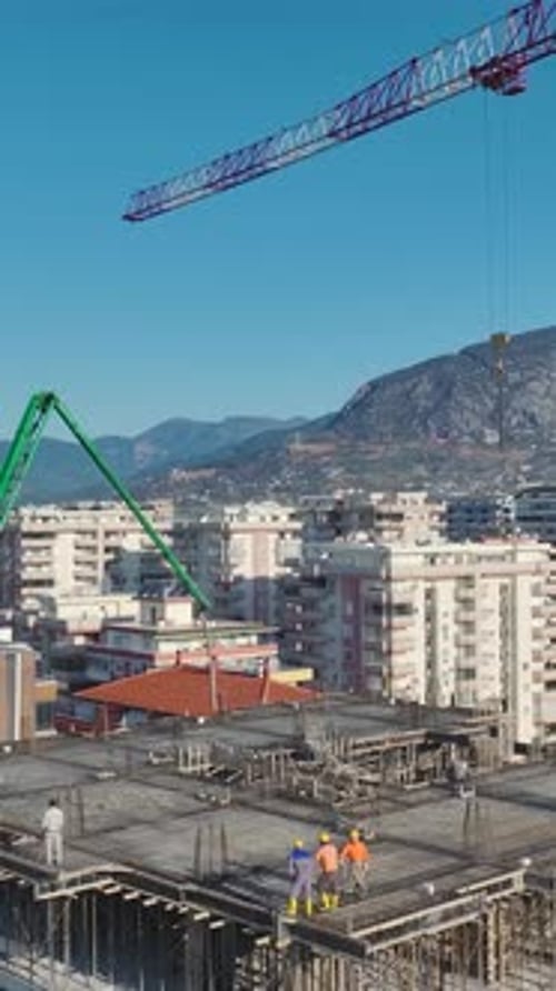 Vertical Video of a Crane Erecting Metal Beams While Workers Build Walls and Lay Concrete