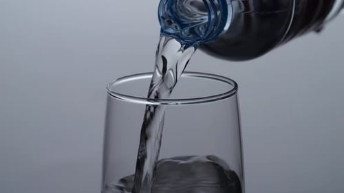 Close Up Of Drinking Water In A Bottle Being Poured Into A Glass On The Light White Background