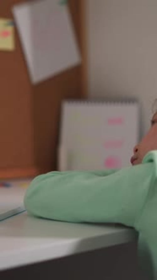 Unhappy Little Schoolgirl Leans on Desk While Does Homework