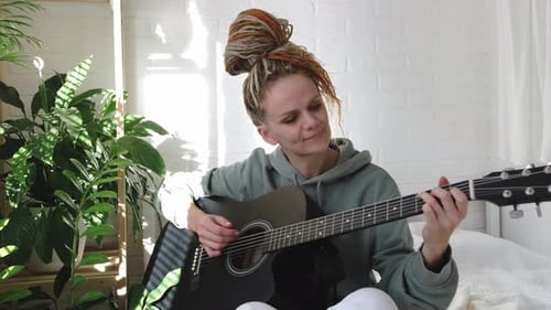Woman Plays Guitar and Smiles in Bedroom