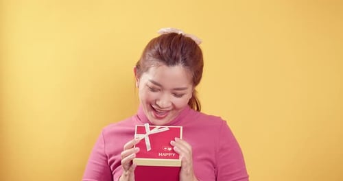 Smiling Woman Holding Birthday Present on Yellow Background