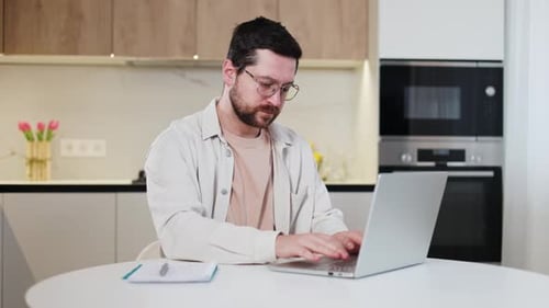 Konzentriertes männliches Tippen auf dem Laptop, während sie in persönlichen Wohnungen sitzen