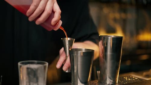Bartender Pouring Red Liquid into Jigger at Bar