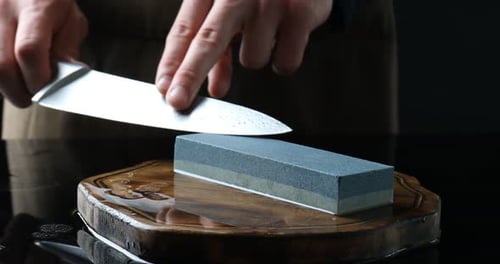 Man sharpening knife with sharpener at mirror table against black background, closeup