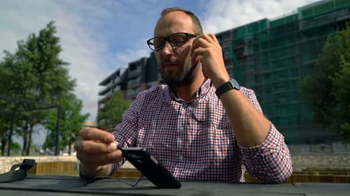 Young man enjoys music on cellphone relaxing on bench in city park