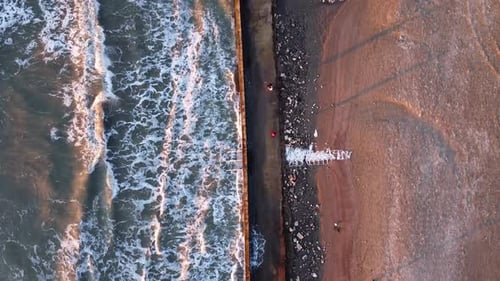 Aerial view above Albanian Coastline with waves crashing against pedestrian pathway