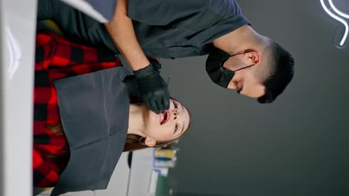 Vertical Video in a Dental Office Male Dentist Examines the Teeth of a Young Beautiful Girl