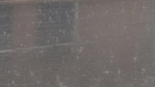 Zeitlupe von Starkregen, der auf eine Asphaltstraße spritzt und dabei Wellen und reflektierende Texturen erzeugt