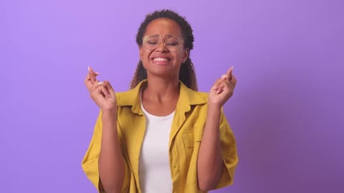 Young Woman Crossing Fingers in Front of Purple Background