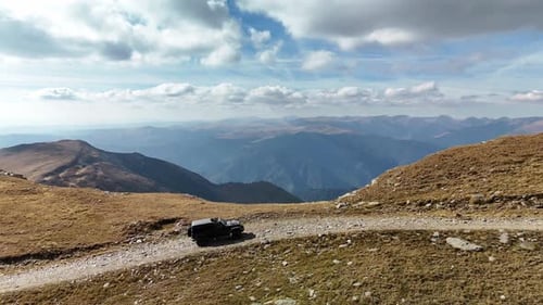 Off-road SUV drives on a remote mountain path with stunning distant views and blue sky above
