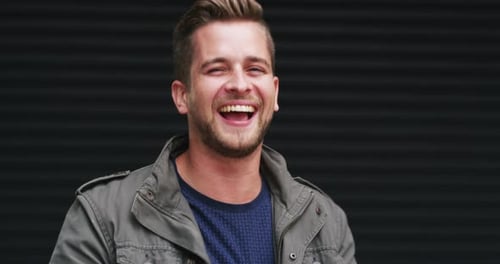A handsome young man dancing and feeling cheerful against a dark background