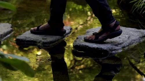 A couple walks across stepping stones on reflective water.