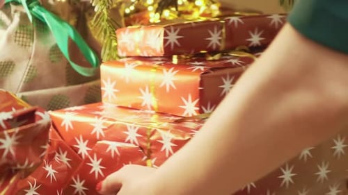 Person legt einen Stapel Geschenke in Schachteln unter den Weihnachtsbaum