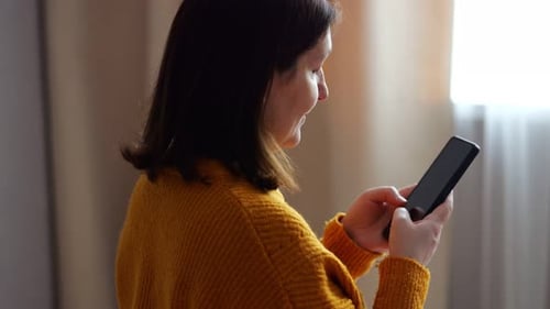 Mujer embarazada que usa un teléfono inteligente en casa