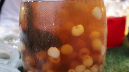 Vendedor de comida mezclando jugo de longan con carne fresca de longan en un gran frasco de vidrio en un puesto de zumos de frutas en w