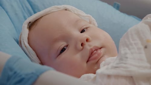 Baby face close up in bathtub swaddled in a cloth.