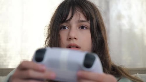 Teenager-Mädchen hält Spielekonsole in der Hand und spielt zu Hause auf einem Sofa