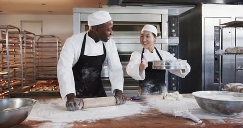 Happy diverse female and male bakers working in bakery kitchen, rolling out dough, slow motion