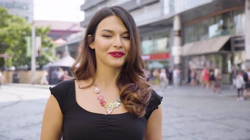 A Young Beautiful Caucasian Woman Talks to the Camera with a Smile in a Street in an Urban Area