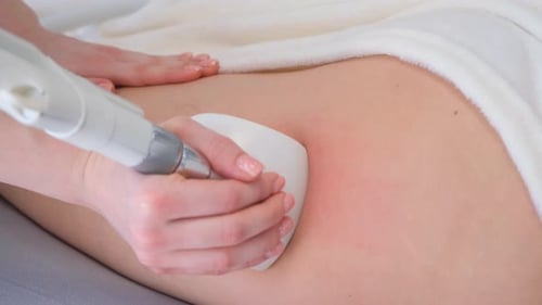 Positiver junger Masseur massiert eine Frau mit einem elektrischen Massagegerät Anti-Cellulite-Wellness-Massage