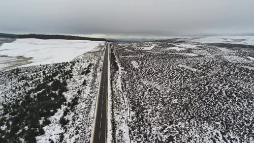Lowering to long road aerial into distance across highland snowy countryside moors